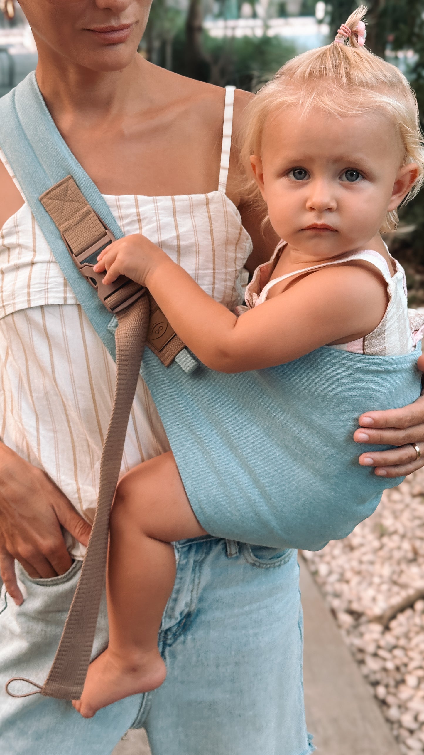 Woman holding a baby in a blue sling outdoors.