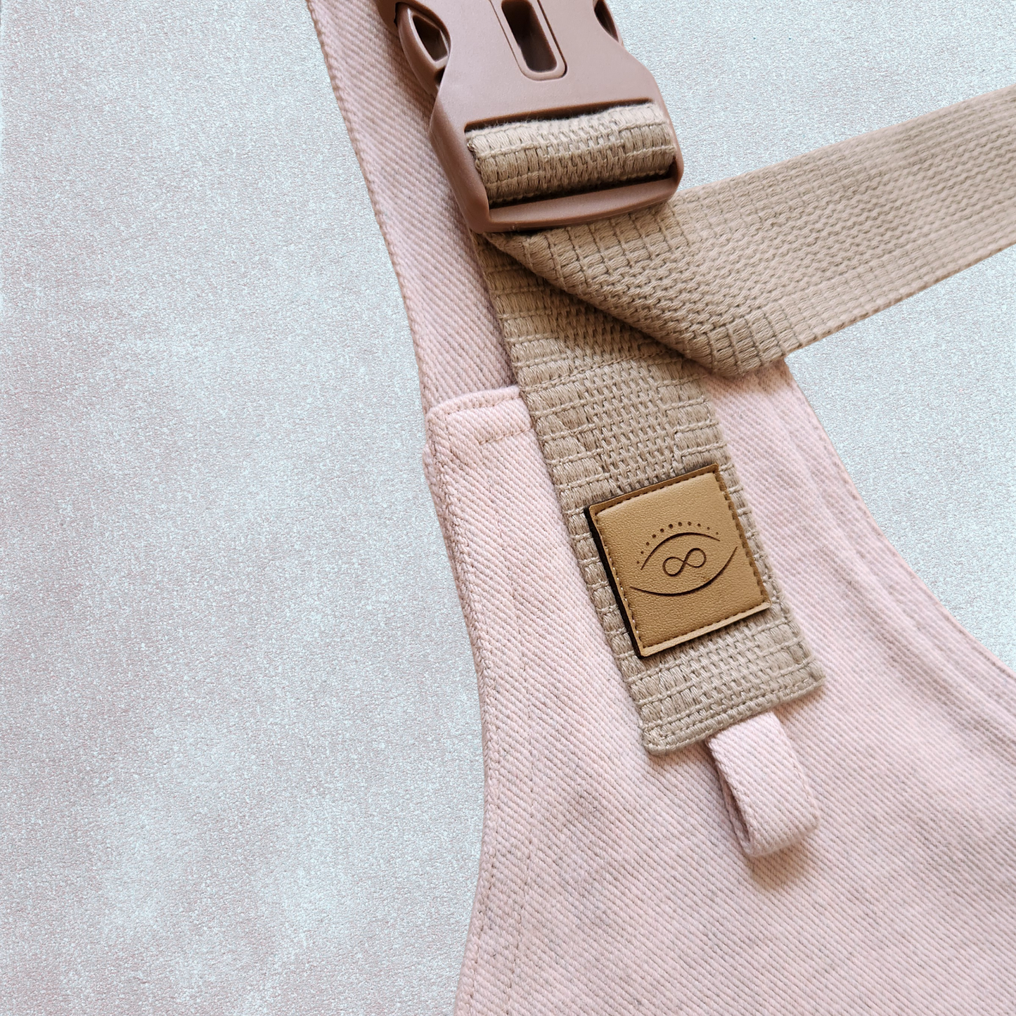 Close-up of a detail on a Denim Pink toddler carrier, showing a plastic buckle and a cotton strap against a denim fabric background.