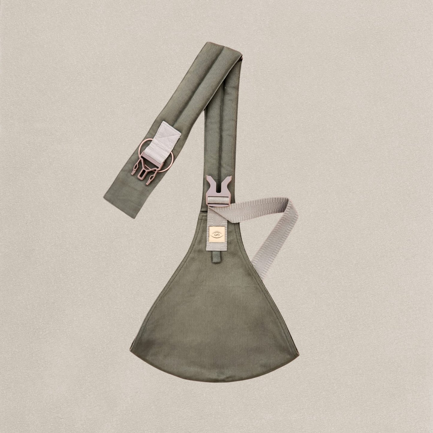 A khaki-colored organic cotton toddler sling carrier with adjustable straps and plastic buckles laid out flat on a light background.