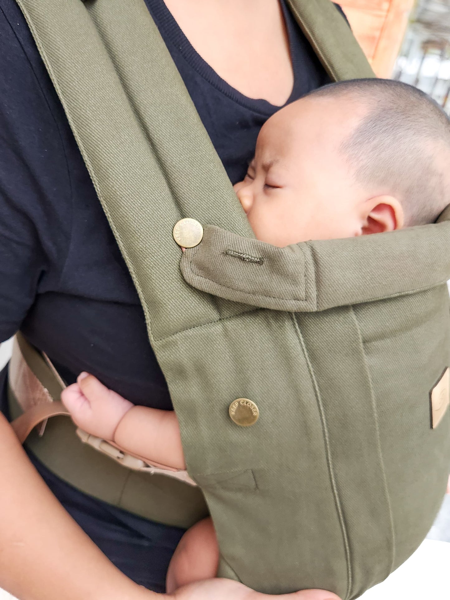 Baby sleeping in an Khaki green baby carrier.
