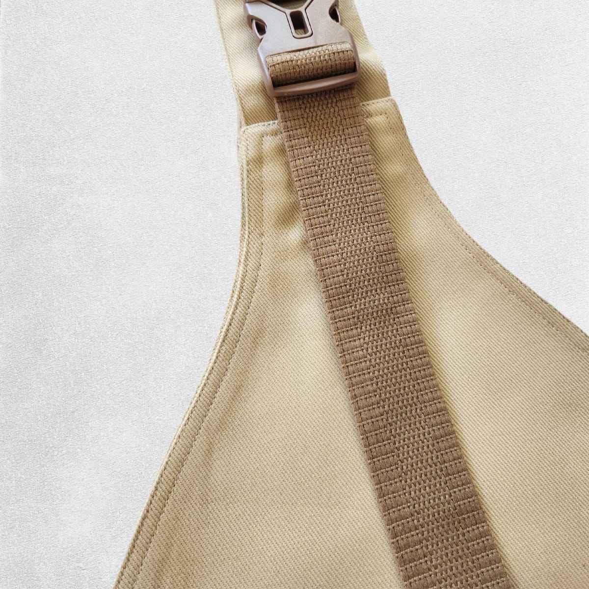 A beige toddler carrier with adjustable straps and a buckle, laid flat on a textured background.