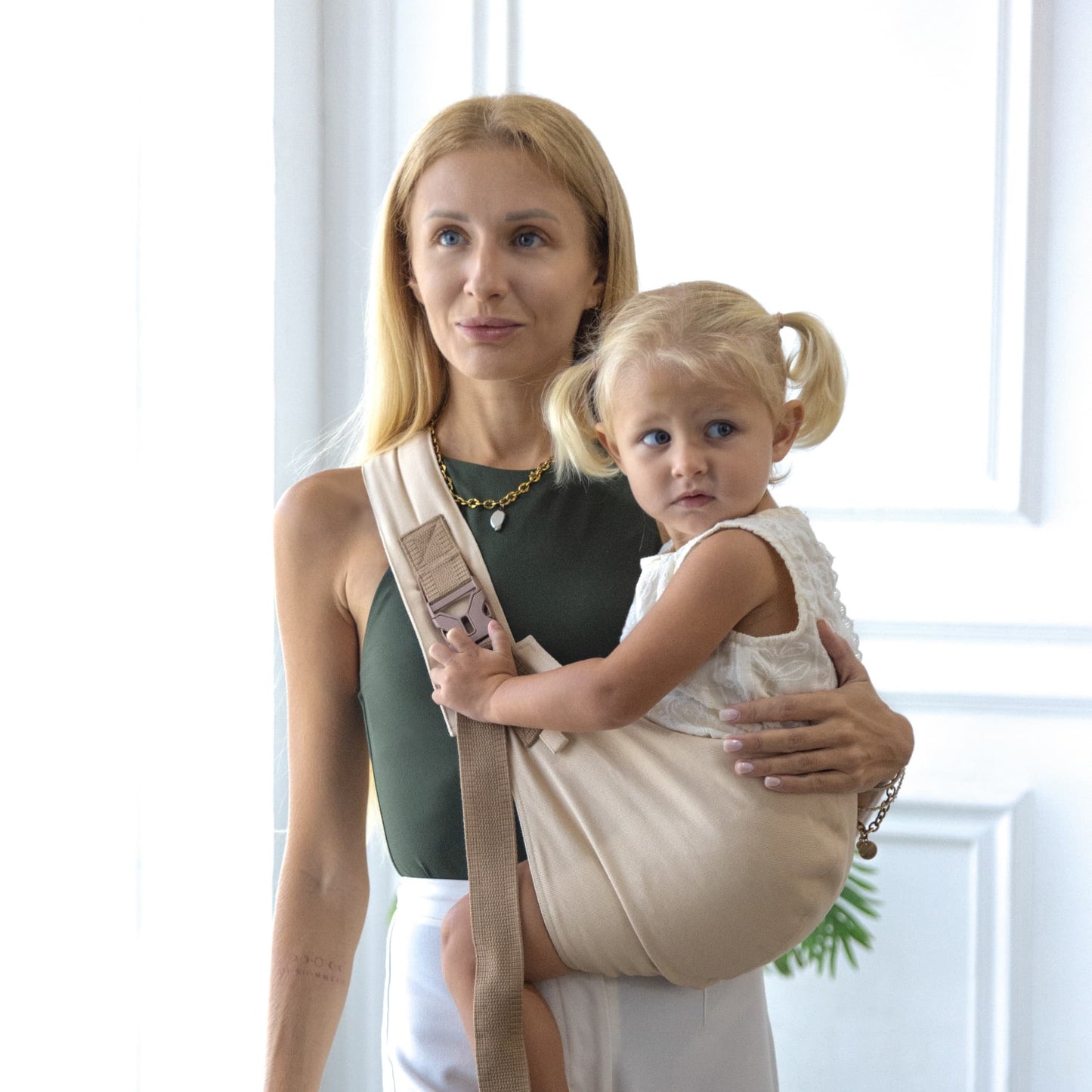 Woman holding a child in a beige baby carrier against a white background