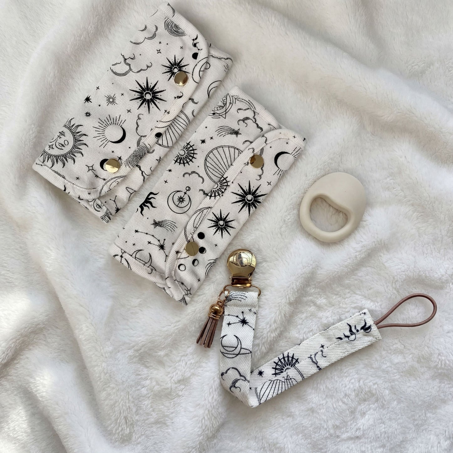 Keep Closer Baby Carrier Teething Drool Pads in sun and moon print with matching pacifier clip and teething ring on white fluffy surface