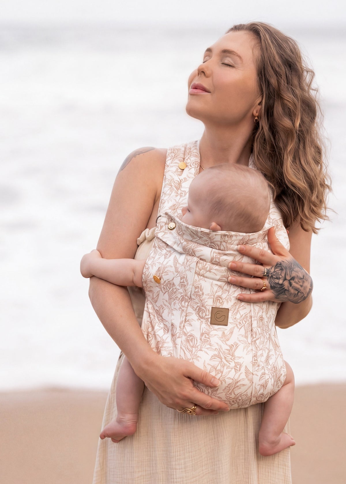 Parent wearing a floral Keep Closer carrier, baby facing in