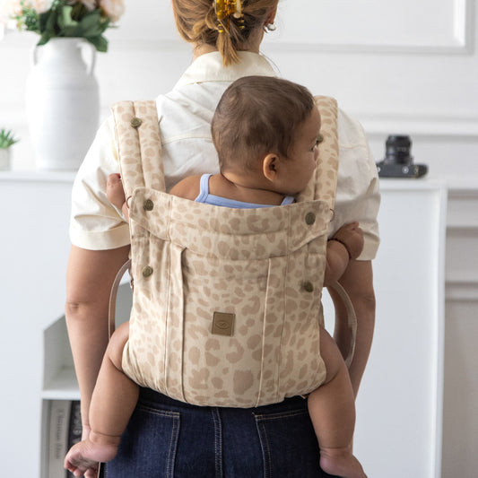 Person carrying a baby in a beige baby carrier with a white background
