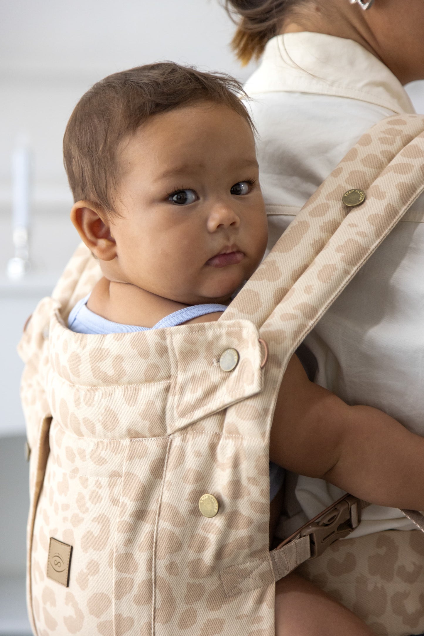 Baby in a beige baby carrier with a blurred background