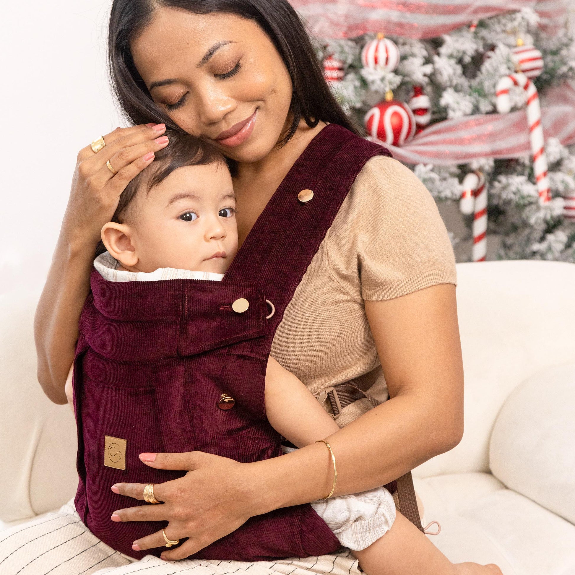 Woman holding a limited edition maroon baby carrier with a Christmas tree in the background