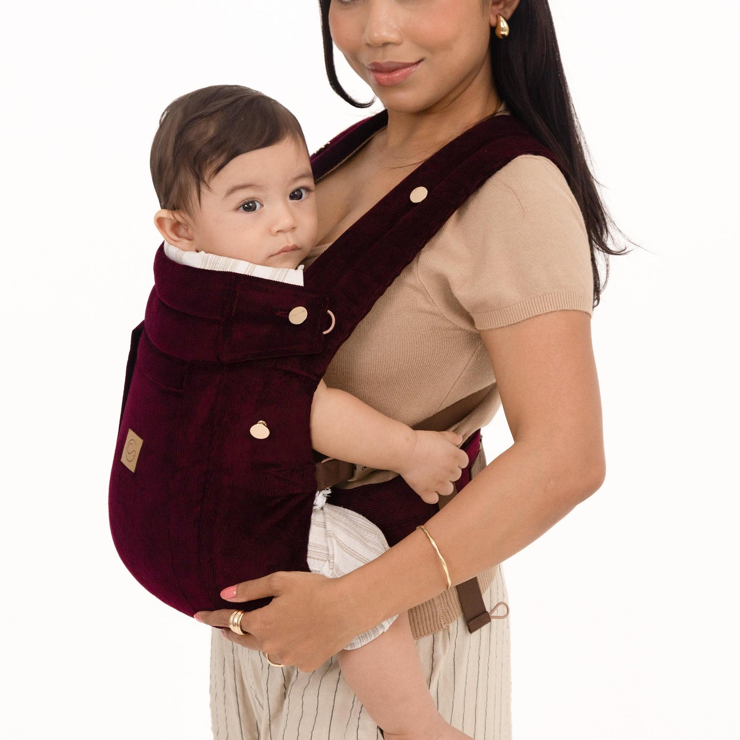 Woman holding a baby in a limited edition maroon baby carrier against a white background