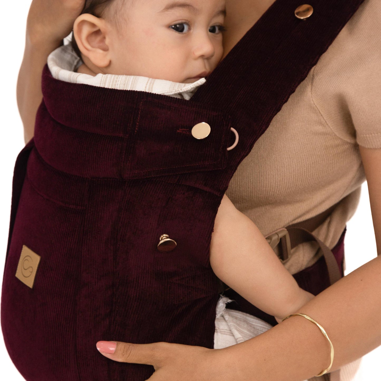 Woman holding a baby in a maroon baby carrier.