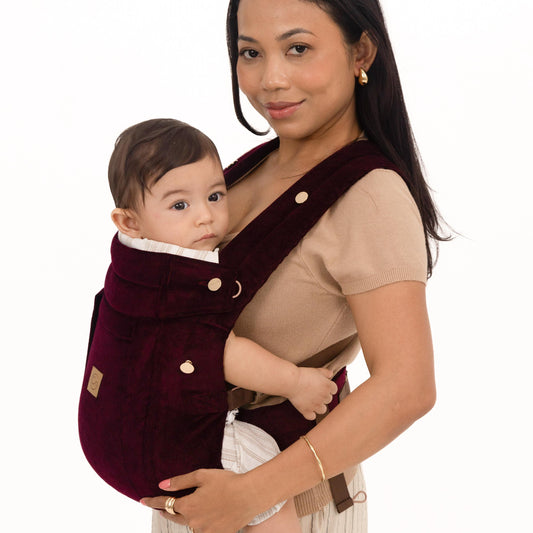 Woman holding a baby in a Maroon baby carrier against a white background
